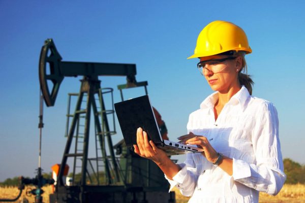 Женщина в каске на фоне нефтяной вышки
